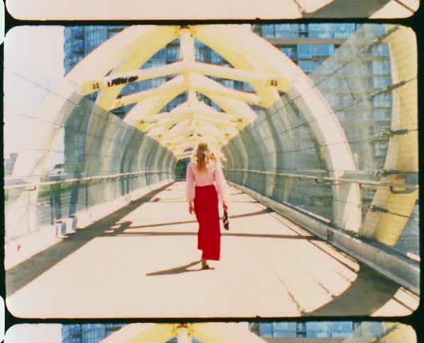 A woman twirls and looks back as she walks across a pedestrian bridge on a bright sunny day