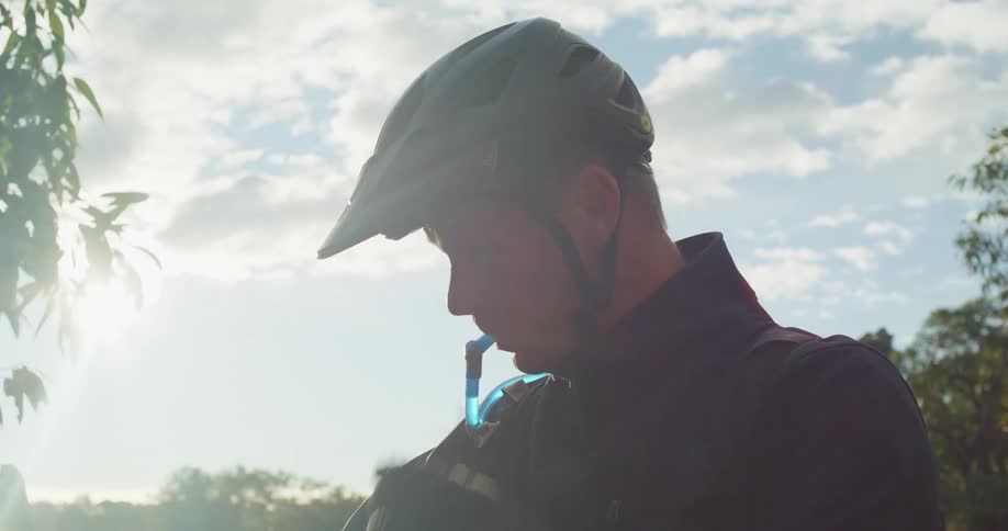 A man takes a drink from his hydration pack as the wind blows leaves and branches around him