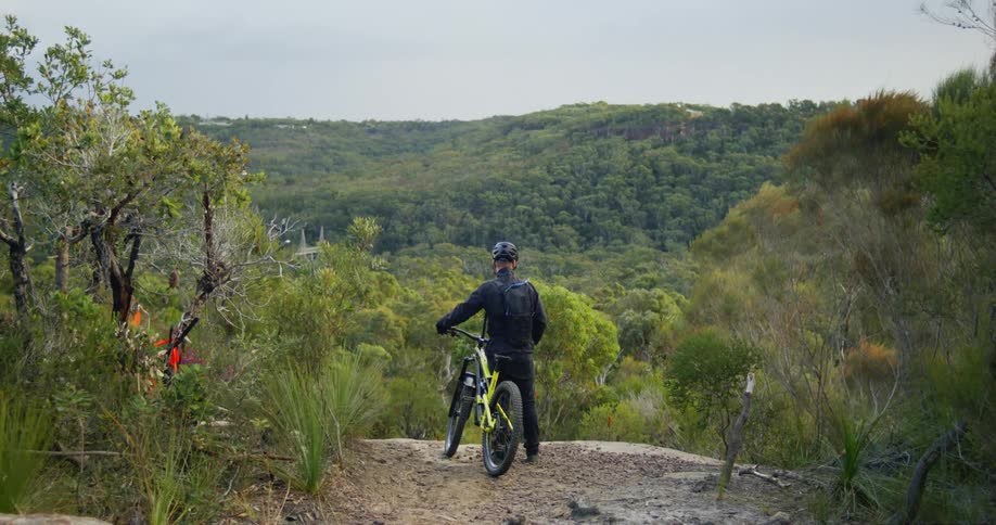 A man standing next to his bike overlooking a forest