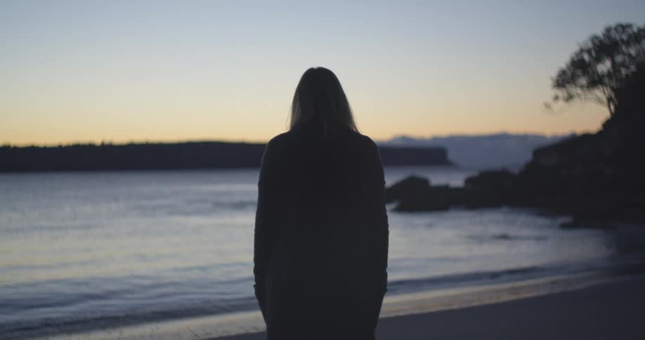 A silhouette of a person on a beach with the ocean sky and clouds in the background