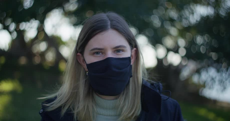 A woman is standing outside wearing a black face mask