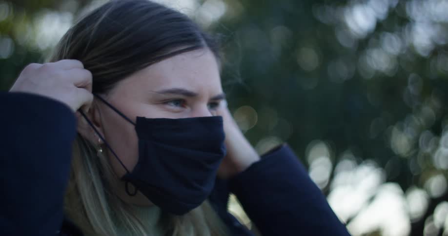 A woman putting on a black face mask outside