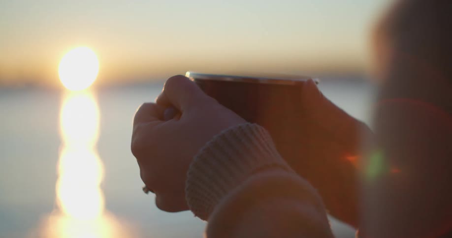 A woman is holding a cup outdoors at dusk
