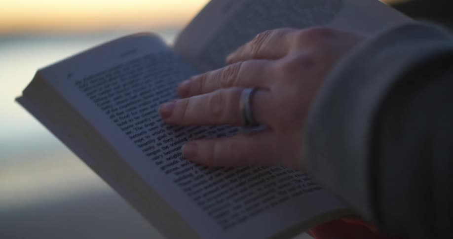 Woman reading a book outdoors in front of a lake at sunset