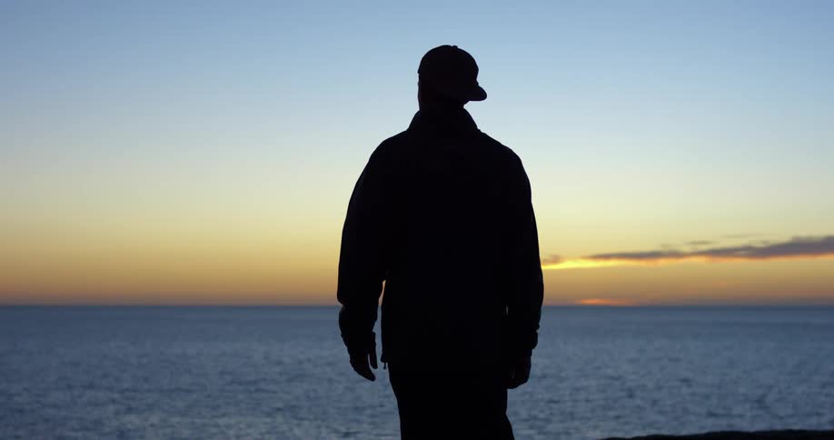 A man looks out over the ocean while standing on the coast at sunset