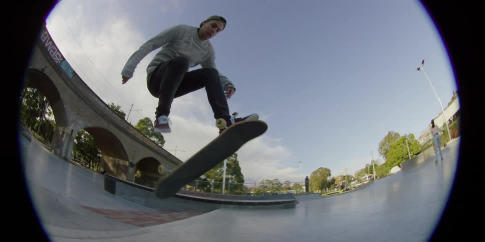 A person with a hat skating on a skateboard on a skate park with trees the sky and clouds in the background