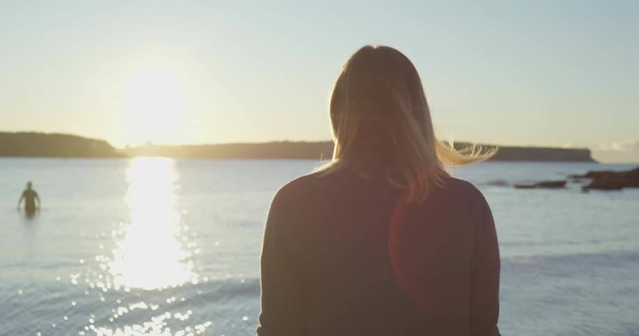 A woman looks out over a bay while standing on its shore during the day