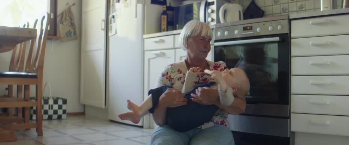 Grandmother sitting in the kitchen floor with her grandson on her hands