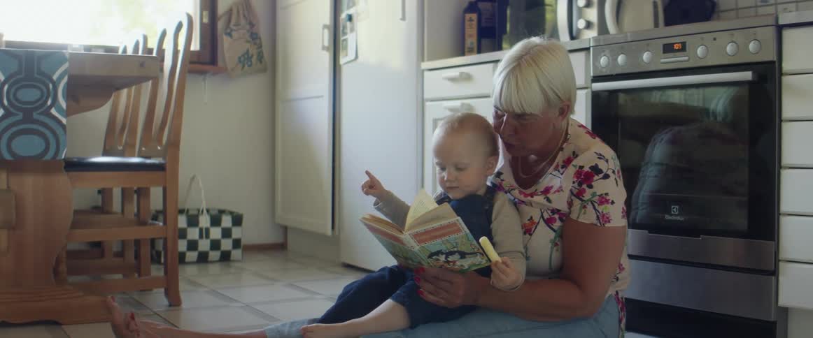 A grandma reads to her grandson while sitting on the kitchen floor