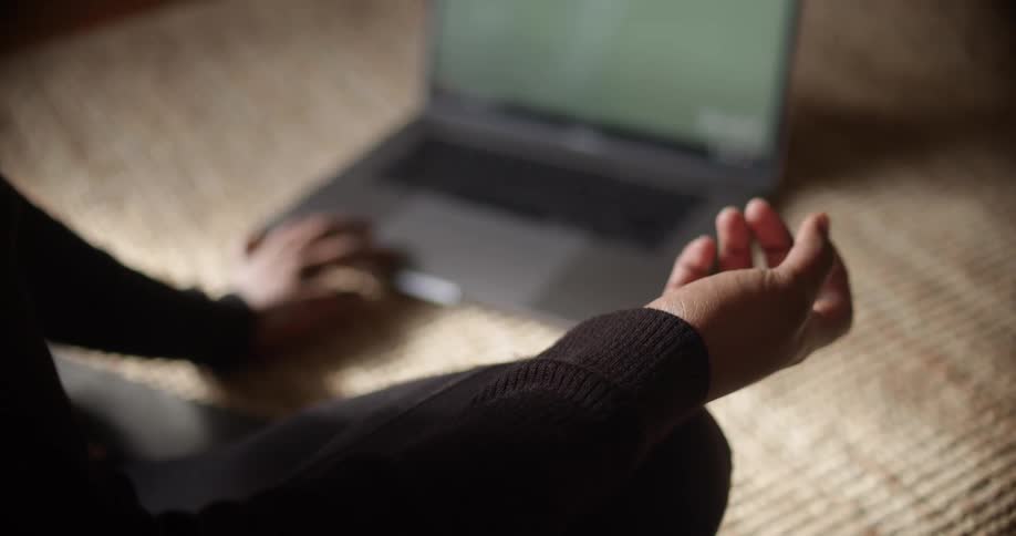 A woman meditating on the floor next to a laptop
