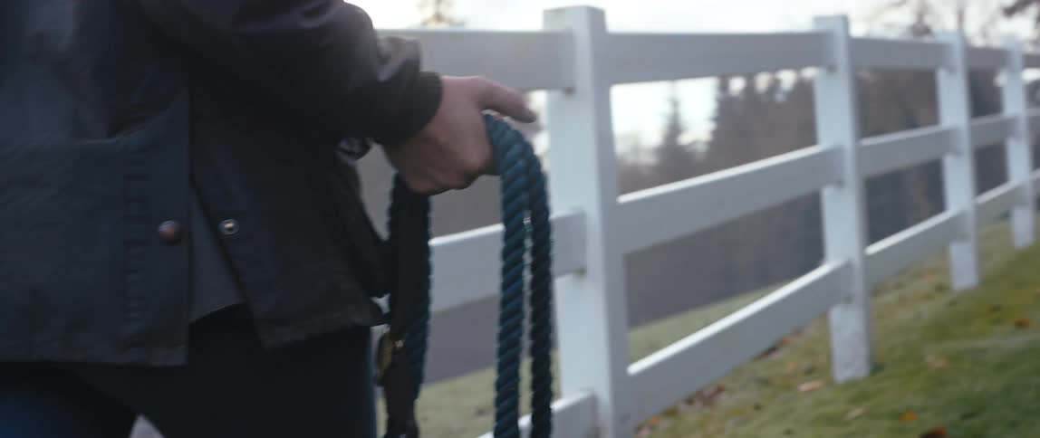A person walking next to a fence holding a lead rope