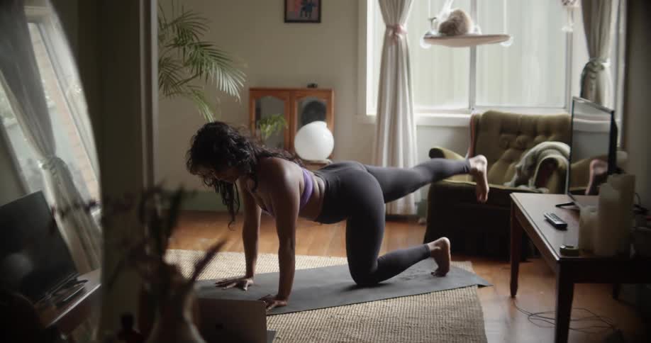 A woman does exercise on a yoga mat in the living room of a house during the day