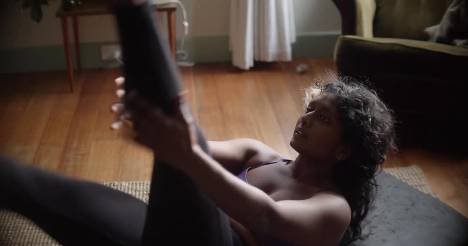 Young woman wearing sports clothes stretches over a mat on the floor of the living room