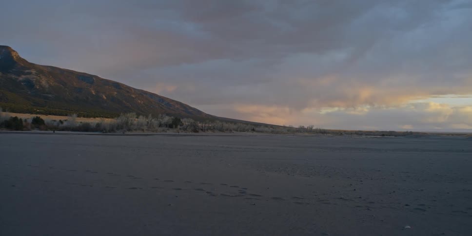 Sunlight glows yellow on the clouds above hills and barren land