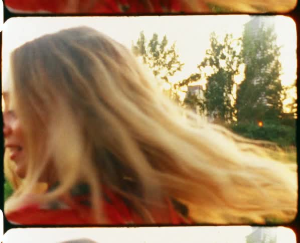 Young blonde woman wearing a colorful dress modeling in a grass field at sunset