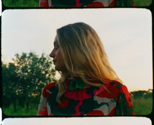 Young blonde woman wearing a long colorful dress on a field at sunset