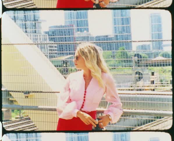 A woman with sunglasses on an overpass with buildings the sky and clouds in the background