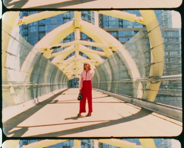 A woman poses on a pedestrian bridge leading to a high rise building