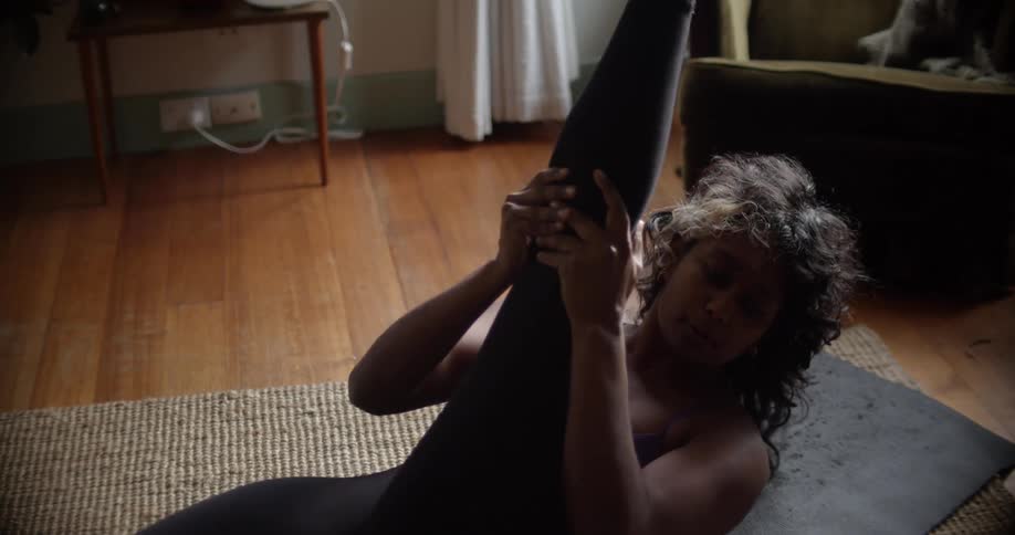A woman in a room exercising on the floor with a wall and window in the background