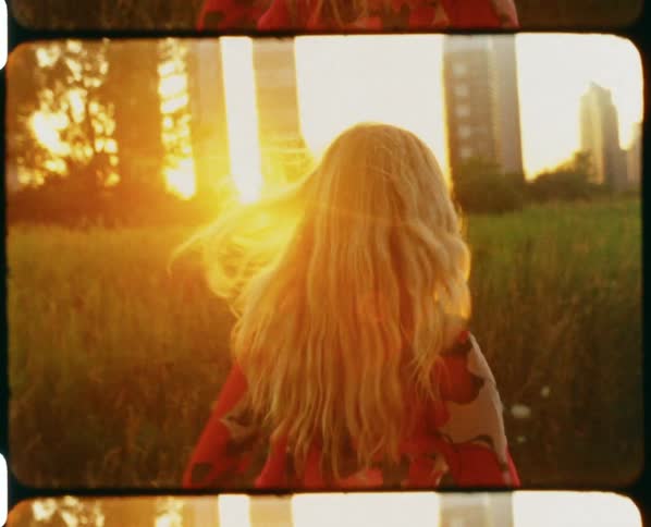Young blonde woman wearing a colorful dress running in a field at sunset