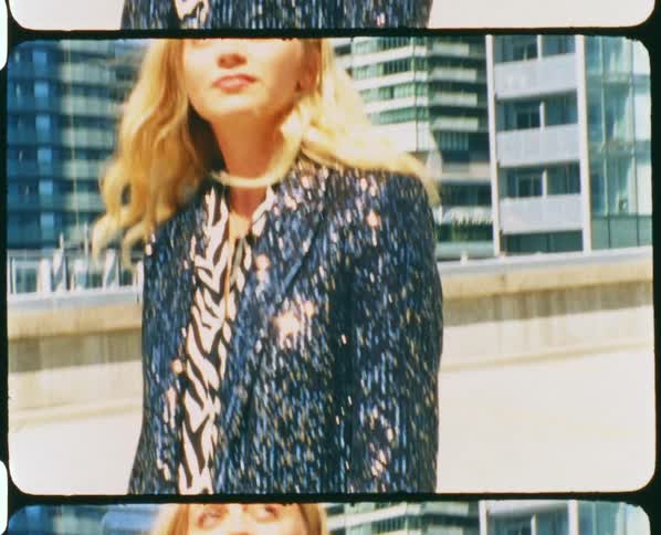 A woman in a glittering suit stands atop a parking age in a metropolis during the day