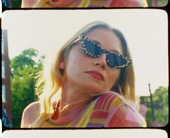 Blonde woman poses wearing sunglasses on bridge over train tracks with skyscrapers in background
