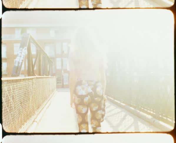 A woman with sunglasses walking in an overpass with a handrail with a building in the background