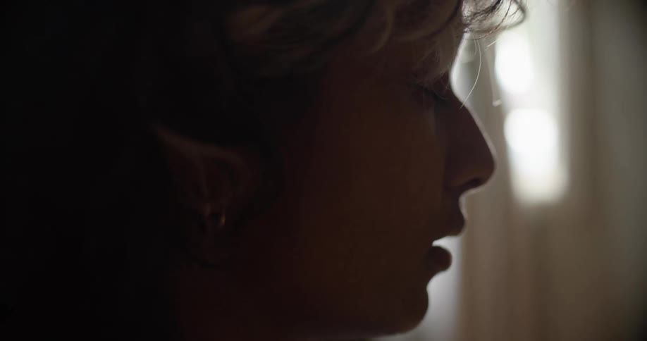 Close up of a woman standing in a dimly lit room with her eyes closed