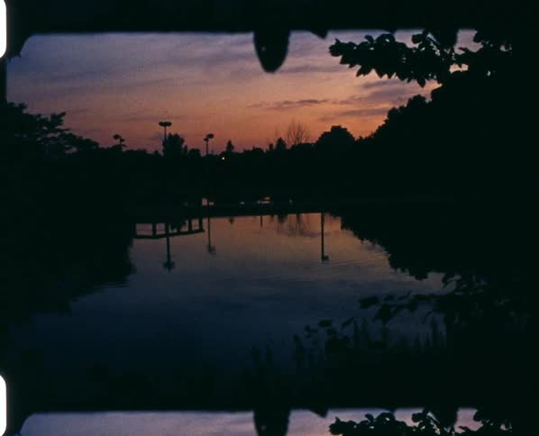 A pond surrounded by trees and plants with the sky and clouds in the background