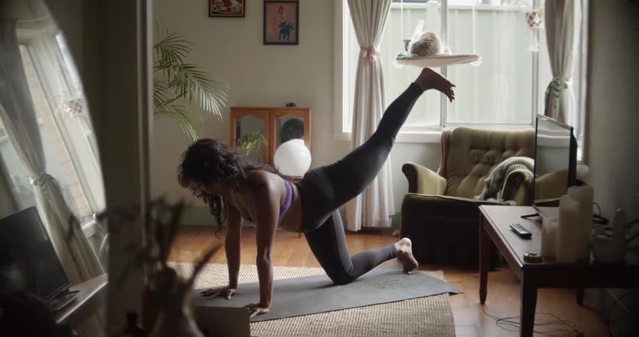 A woman is on a yoga mat on the floor doing stretches