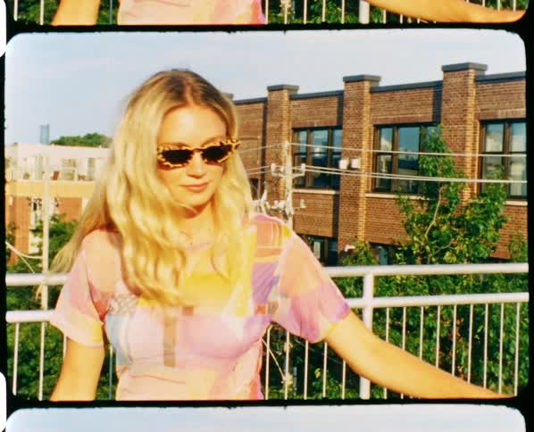 A woman spins and stares into the camera while walking across an urban pedestrian bridge