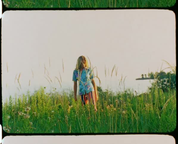 A woman is standing in a farm land with a water body visible in the background