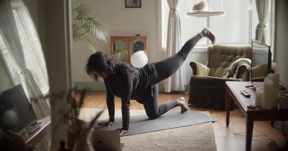 A woman in a room exercising on the floor with a wall and window in the background