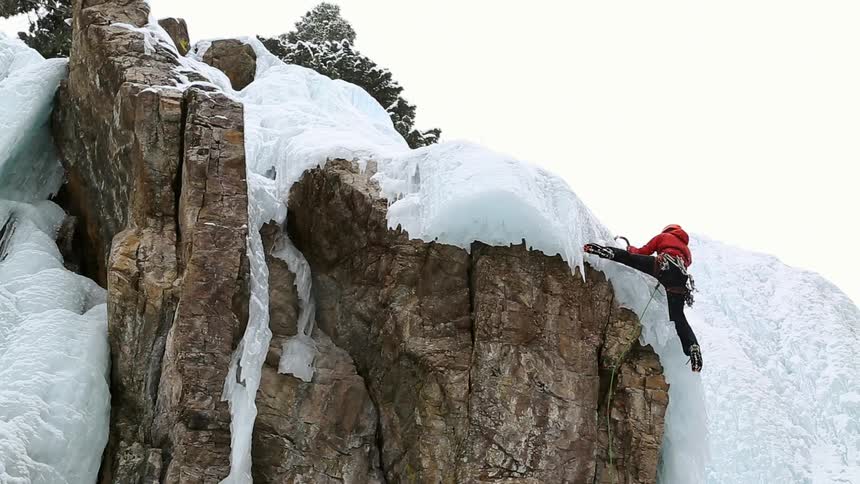 A man is climbing up a cliff covered with snow
