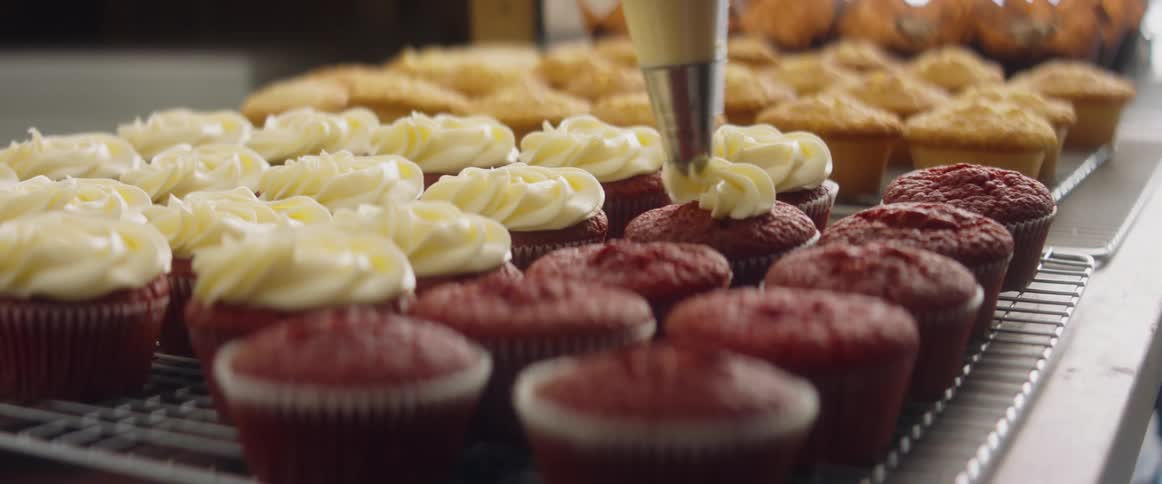 A baker piping frosting onto cupcakes on a metal rack