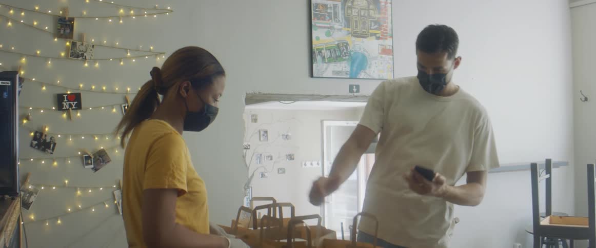 A man walks into a cafe and picks up a prepared food order in a brown paper bag