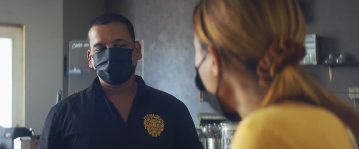 A barista in a coffee shop hands over a take out bag to a customer