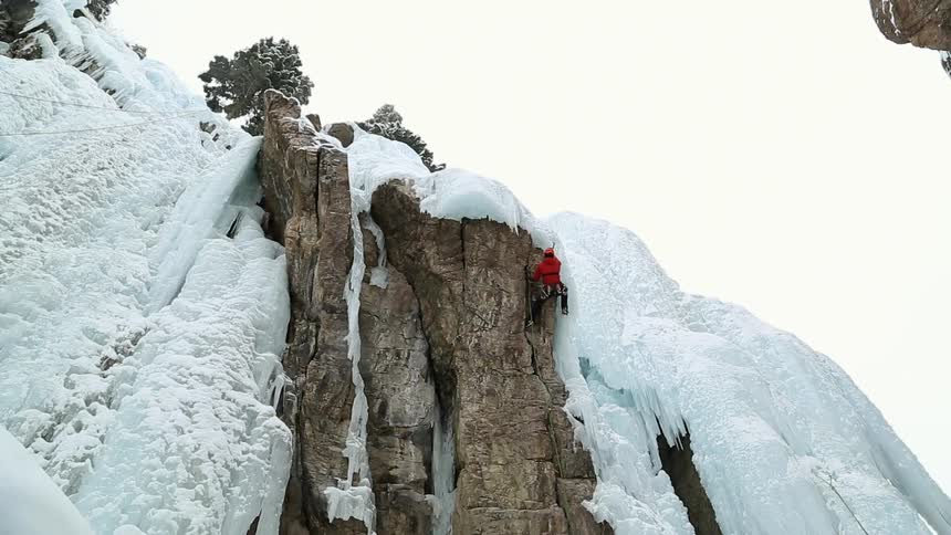Rock climber nearing the top of his destination chipping away at ice with his pick