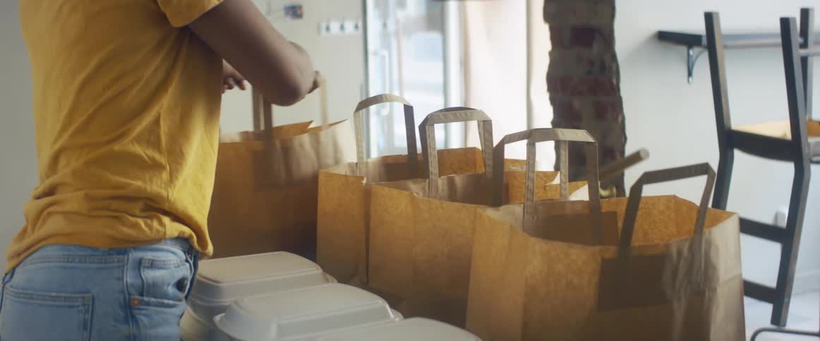 A woman places foam food containers into paper bags and hands them out