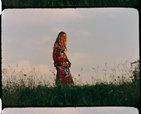 Young woman wearing a colorful dress on a grass field at sunset