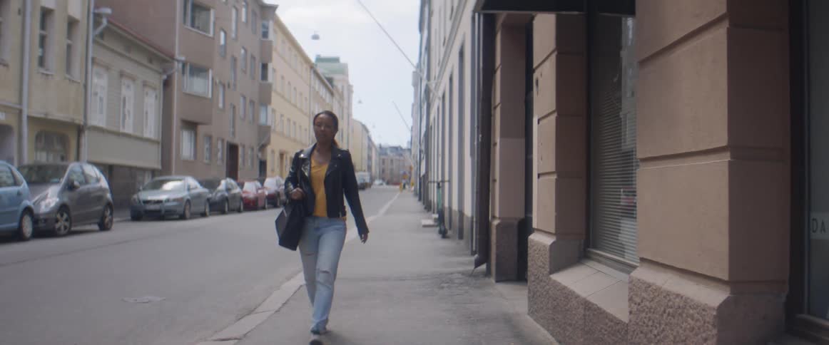 A woman walks down a city street lined with parked cars