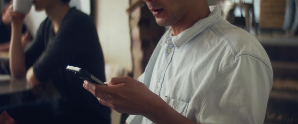 A man takes a swig from a small class then looks at his cell phone and starts swiping through