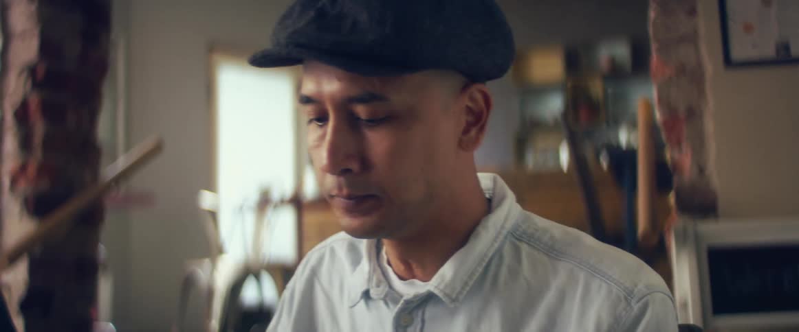 A man sits at a table in a restaurant as another man enters and a woman stands by the front door