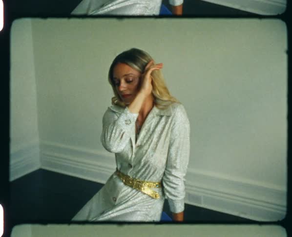 Young blonde woman in a silver dress modelling inside a room caught on vintage film