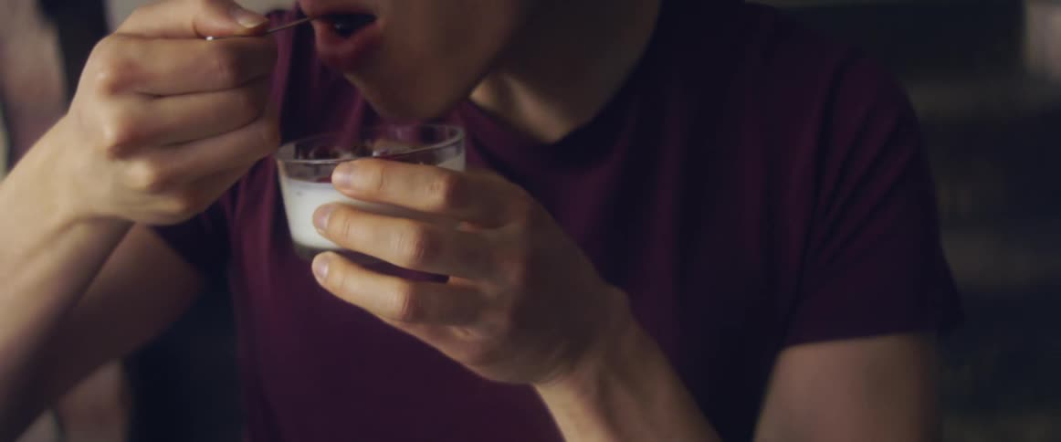 A person in a room eating yogurt with a spoon with a wall in the background