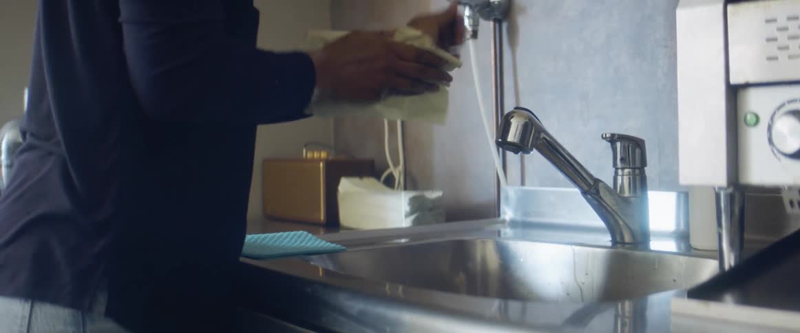 A person washes their hands in a sink and dries them with a paper towel
