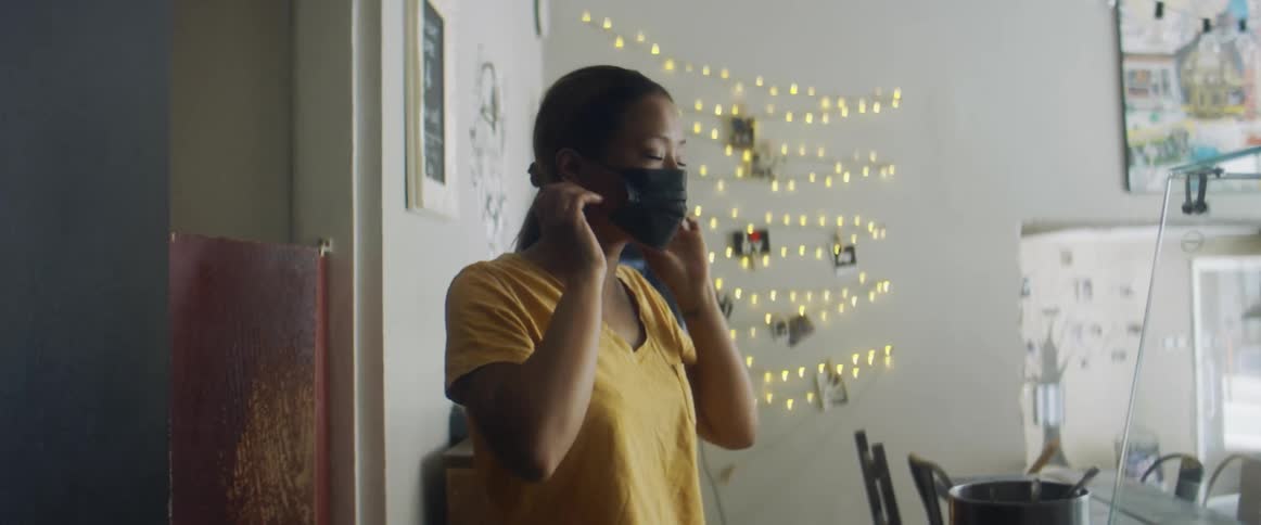 A woman walks into the main room of a business while putting on her face mask