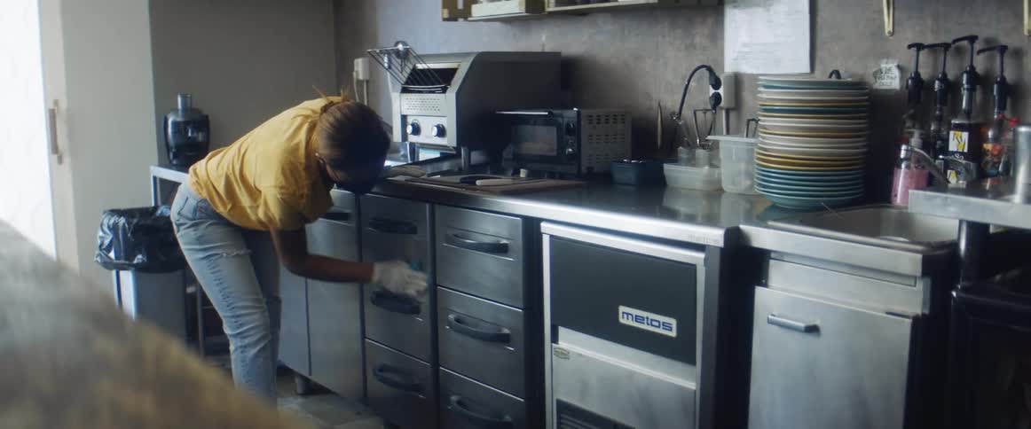 A female employee in a face mask wiping down cabinets in a restaurant kitchen