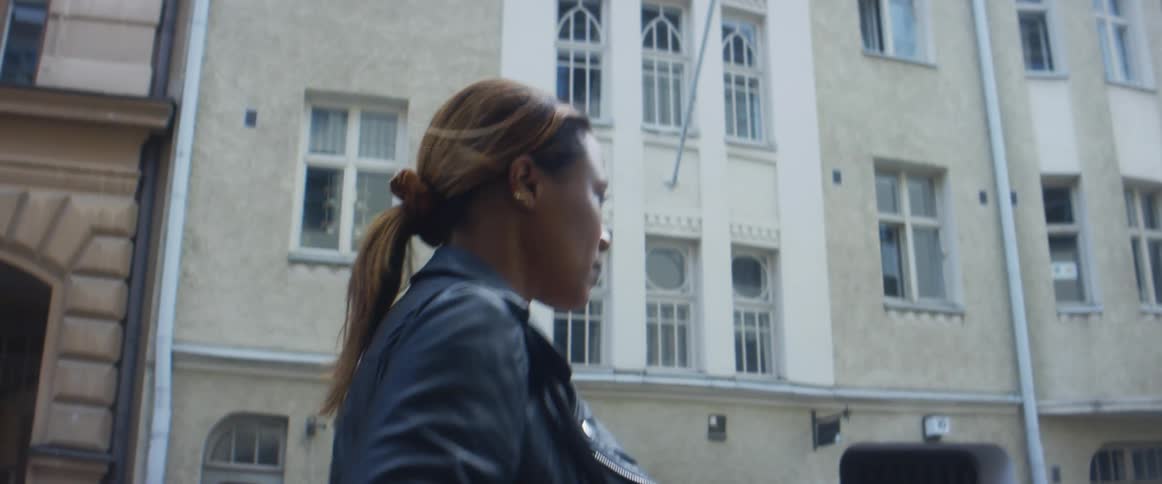 A woman walking on a city street with vehicles with buildings the sky and clouds in the background