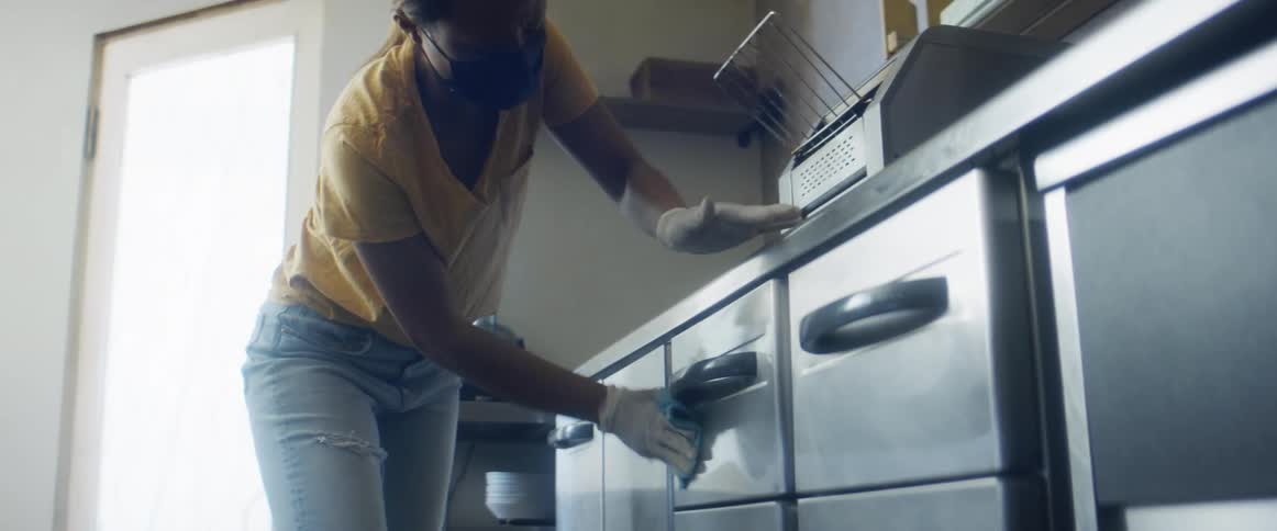 A woman uses a cloth to wipe clean the surfaces of drawers in an industrial kitchen